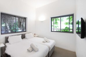 A modern bedroom with two beds, large windows, a flat-screen TV, and a bedside table.