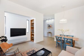 Un salon moderne doté d’un téléviseur à écran plat, d’un coin repas avec des chaises bleues et d’un luminaire suspendu original.