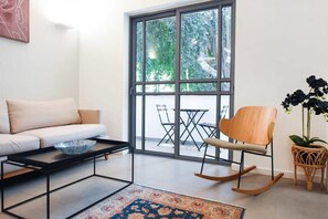 A living room with a sofa, a coffee table, a rocking chair, and a large window with a view of greenery.