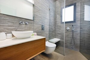 A modern bathroom with a large white sink, a wooden vanity, a toilet, and a glass-enclosed shower area. - Magic Lily in Frug by HolyGuest (Tel Aviv)