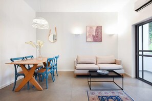 A modern living room with a dining area, a sofa, a coffee table, and a large window. - Magic Lily in Frug by HolyGuest (Tel Aviv)
