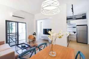 A modern living space with a dining area, kitchen, and a large window providing natural light. - Magic Lily in Frug by HolyGuest (Tel Aviv)