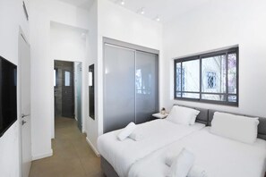 Una habitación de hotel moderna con una cama grande, un vestidor, una mesita de noche pequeña y una ventana con vistas a árboles.