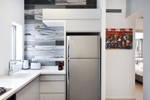 A modern kitchen with a stainless steel refrigerator, a window, and a white countertop. - Magic Lily in Frug by HolyGuest (Tel Aviv)
