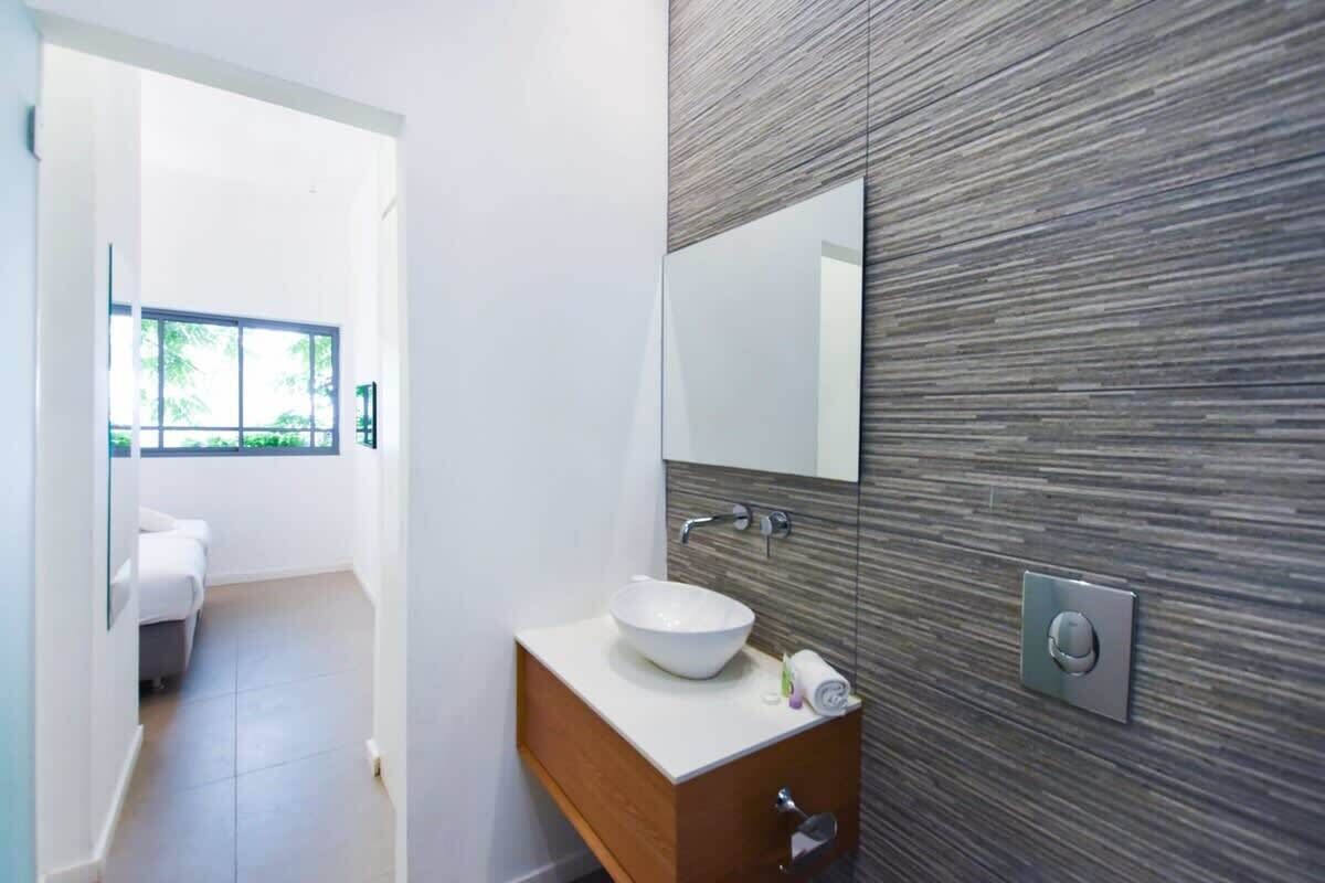 A modern bathroom with a white sink, wooden vanity, and a large mirror.