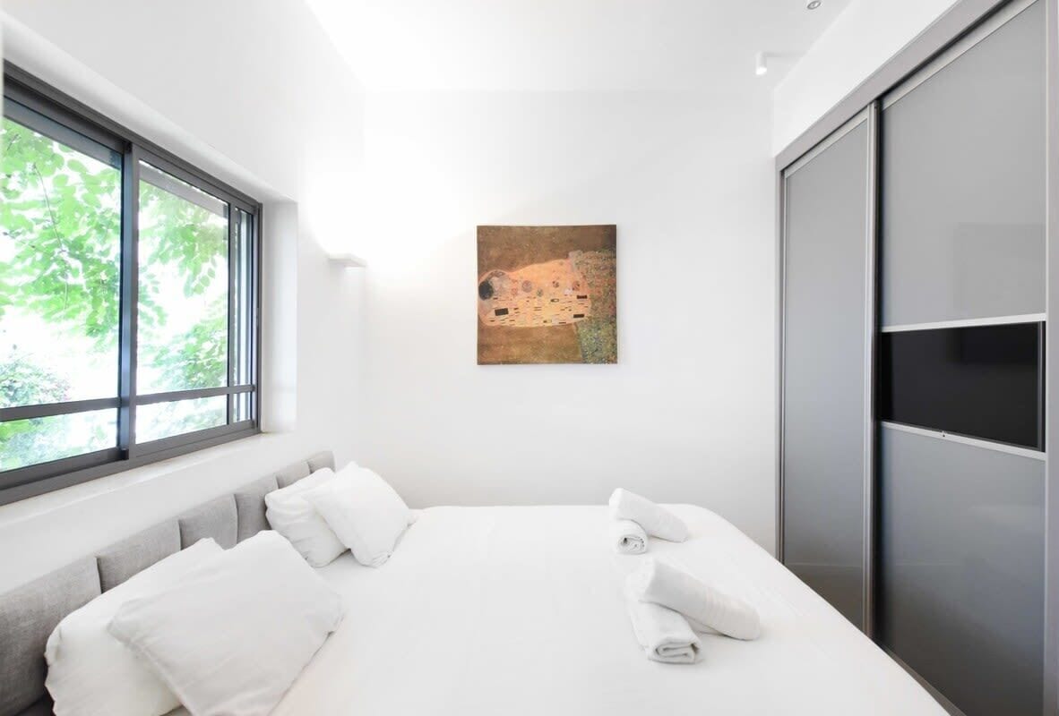 A modern hotel room with a large bed, a window with a view of trees, and a painting on the wall.