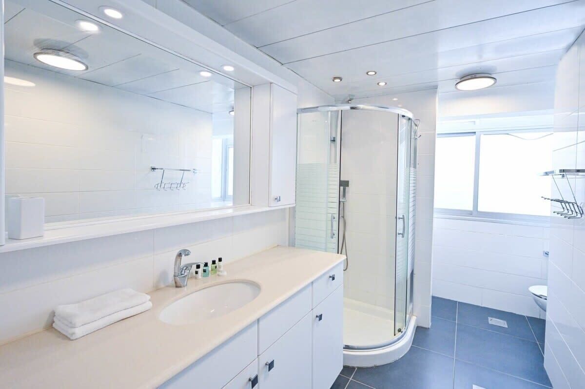 A modern bathroom with a white vanity, a glass shower enclosure, and a large mirror.