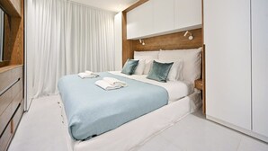 Een opgemaakt bed met een blauwe deken en witte kussens, een houten hoofdbord en een witte inbouwkast.