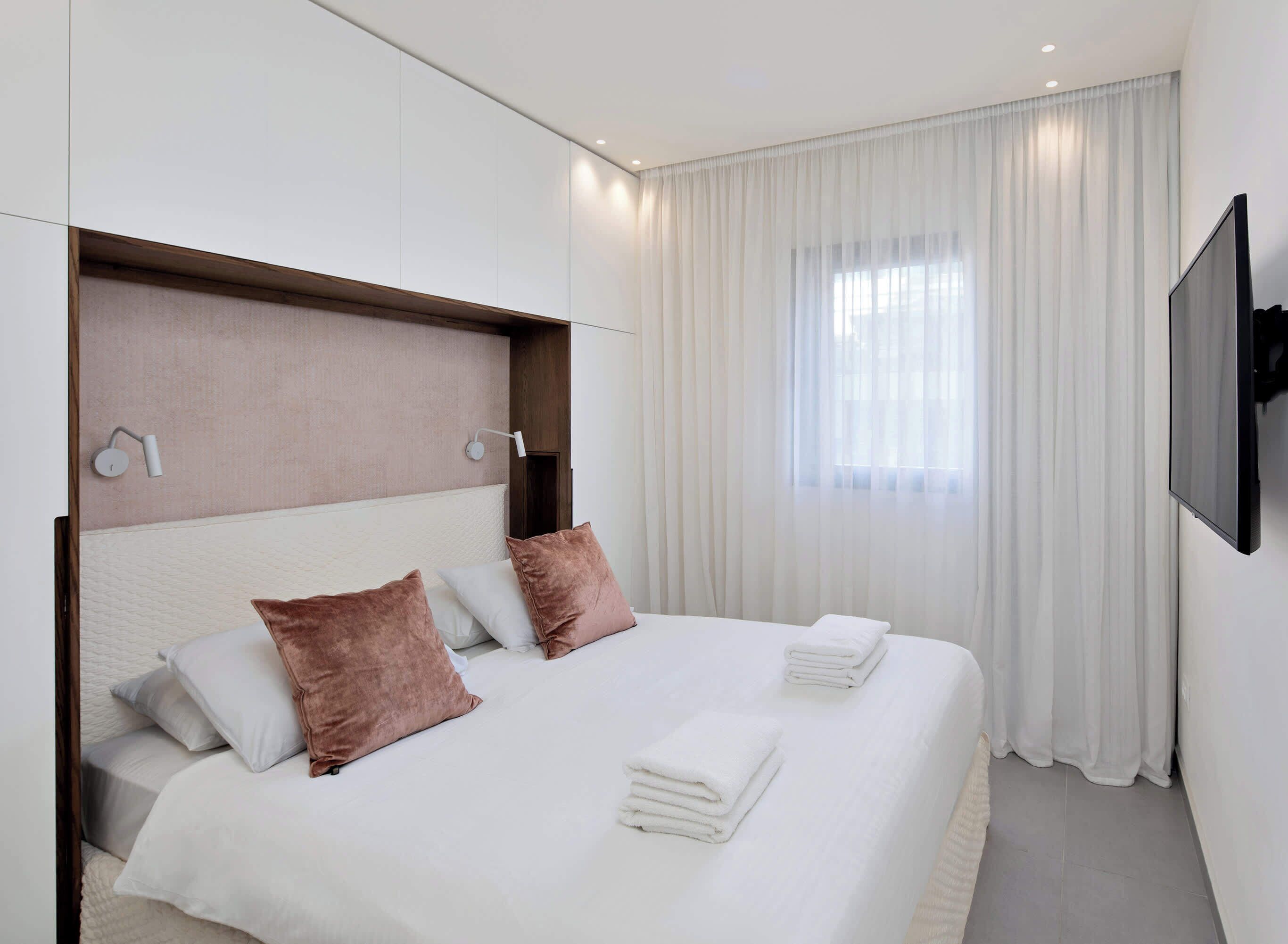 A modern hotel room with a large bed, white bedding, and a flat-screen TV mounted on the wall.