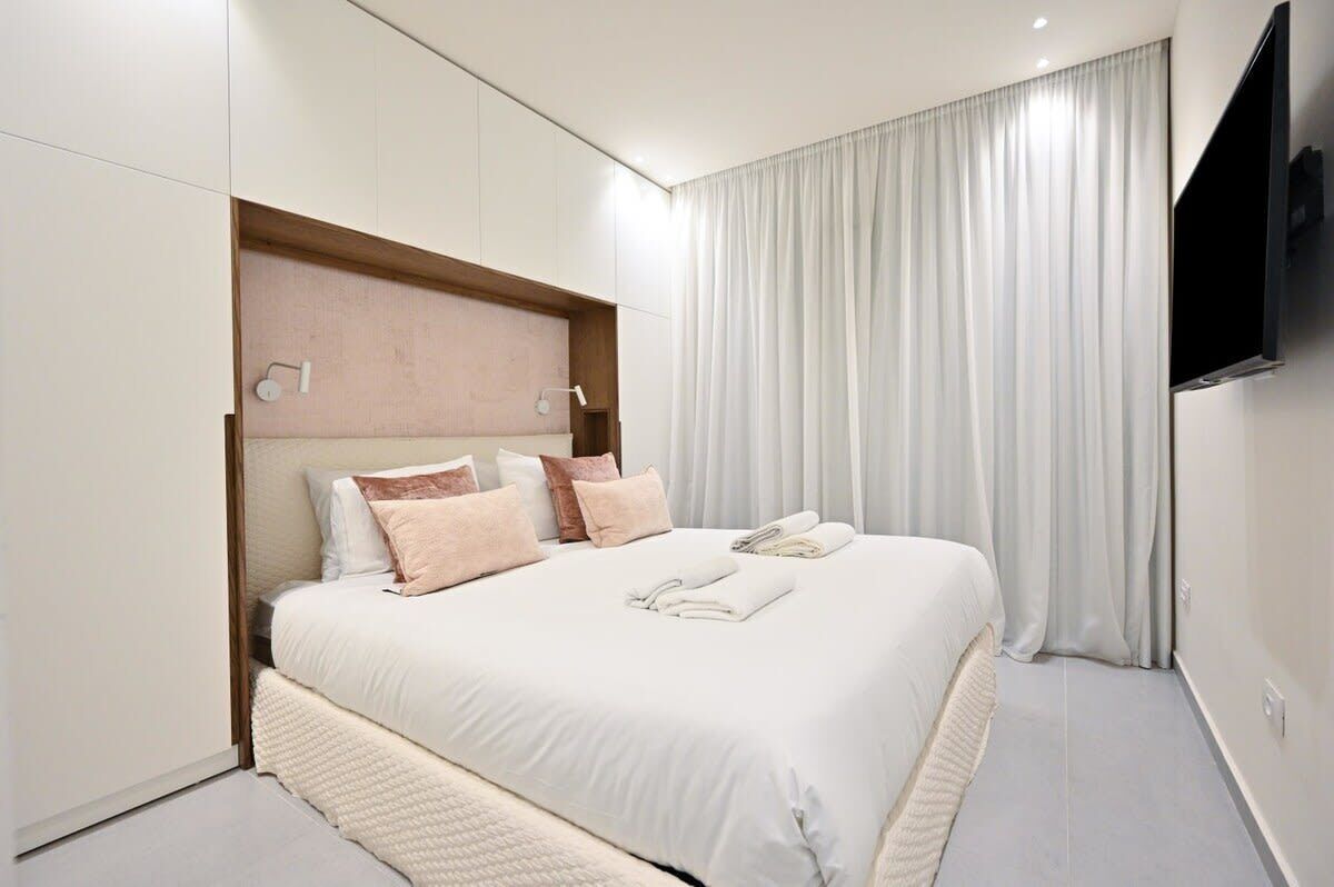 Ein modernes Hotelzimmer mit einem großen Bett, einem flachbildfernseher an der Wand und einem großen Fenster mit Vorhängen.