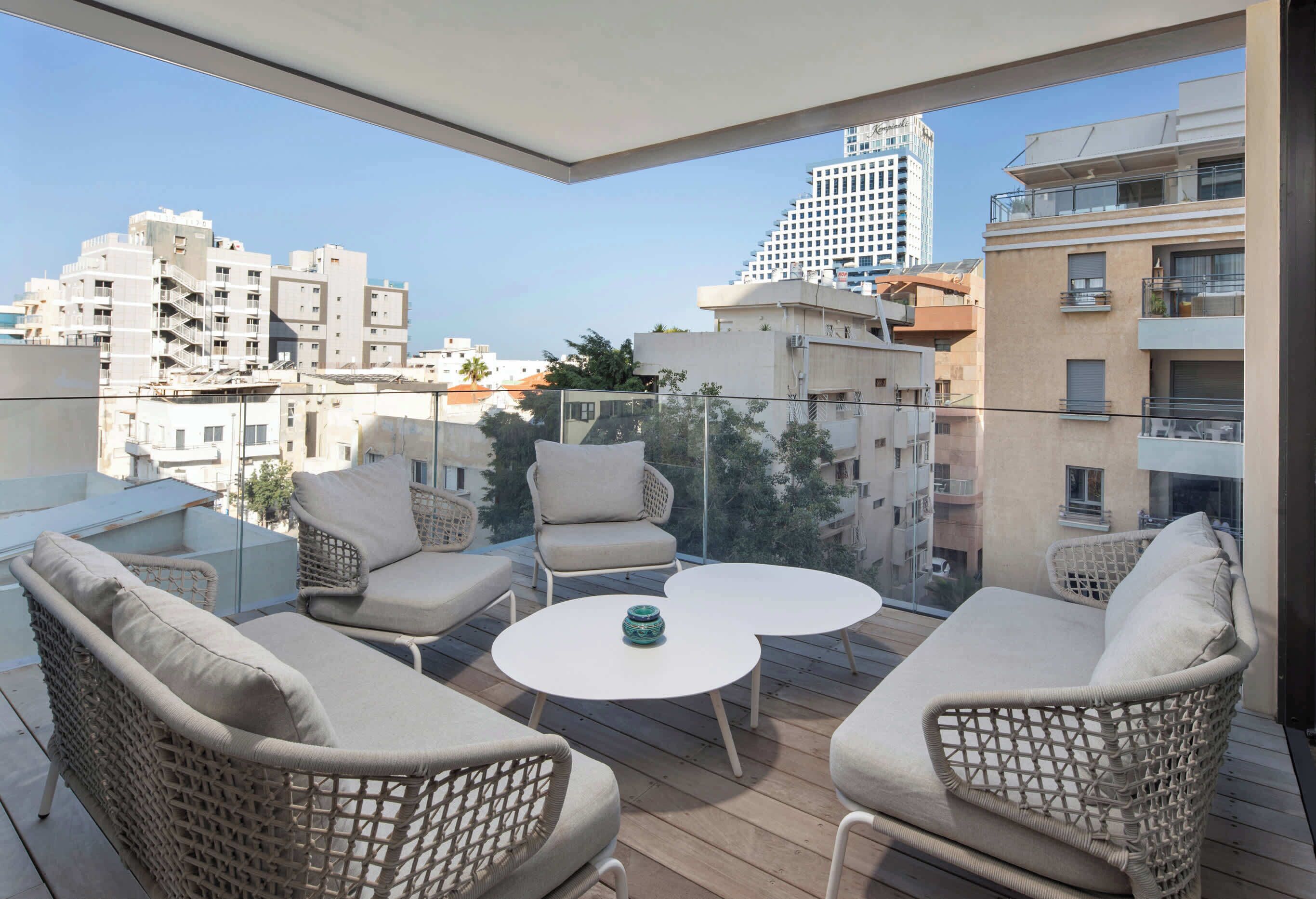 A balcony with wicker furniture, a round table, and a view of city buildings.