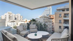 Een balkon met rieten meubilair, een ronde tafel en uitzicht op stadsgebouwen.