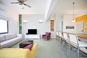 Ett modernt vardagsrum med en soffa, en tv, ett soffbord och en matplats med stolar.