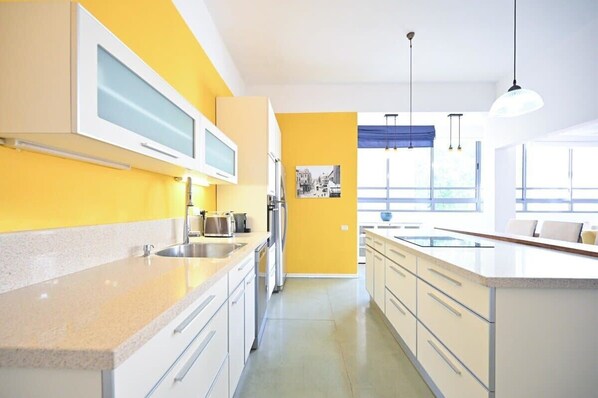 A modern kitchen with yellow walls, white cabinets, and a large window providing natural light.