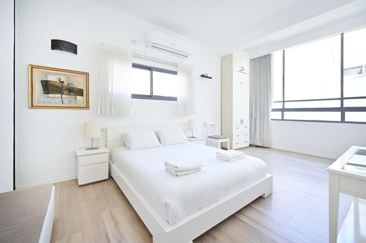 Une chambre moderne avec un grand lit, des murs blancs et une grande fenêtre.