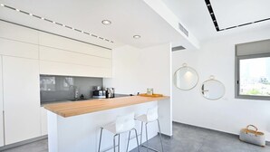A modern kitchen with a wooden countertop, white bar stools, and a window with a view. - Luxury 3BR Beachfront Penthouse by HolyGuest (Tel Aviv)