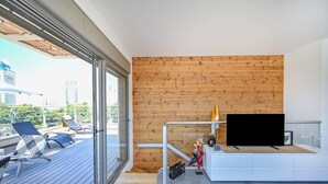A modern living room with a wooden wall, a TV, and a balcony with sun loungers. - Luxury 3BR Beachfront Penthouse by HolyGuest (Tel Aviv)