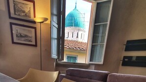 A modern room with a glass table, a brown sofa, and a view of a blue-domed building through an open window. - Apartment in the Center of Florence With a View (Florence)