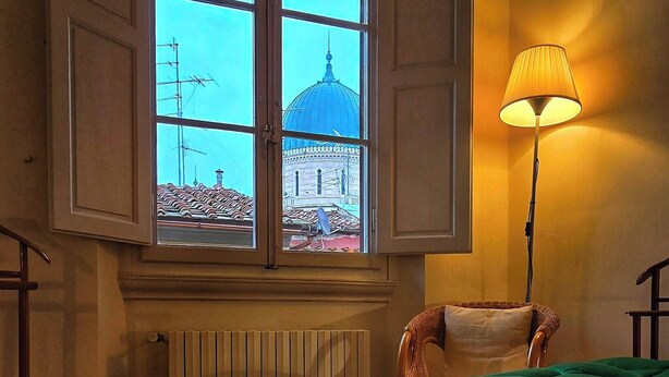A room with a large window, a radiator, a green bedspread, and a floor lamp. - Apartment in the Center of Florence With a View (Florence)
