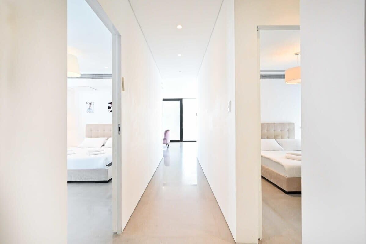 A modern hotel corridor with a minimalist design, featuring a central open space and two bedrooms with beds on either side.