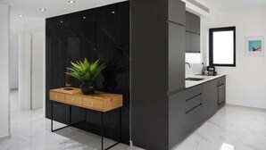 A modern kitchen with a marble countertop, black cabinetry, and a wooden sideboard with a plant. - Outer Space at Hayarkon by HolyGuest (Tel Aviv-Yafo)