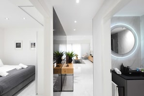 A modern hotel room with a bed, a desk with plants, a round mirror, and a bathroom with a sink and mirror. - Outer Space at Hayarkon by HolyGuest (Tel Aviv-Yafo)