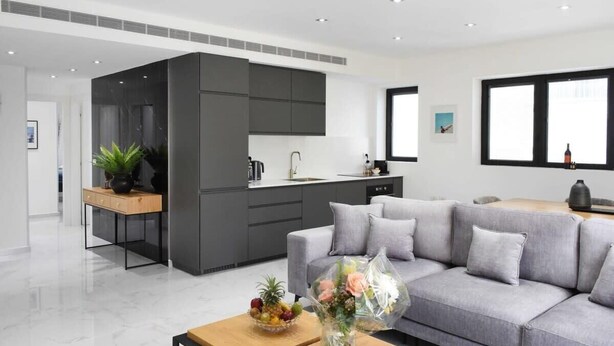 A modern living space with a grey sofa, a wooden coffee table, and a kitchen area with dark cabinets and a white countertop. - Outer Space at Hayarkon by HolyGuest (Tel Aviv-Yafo)