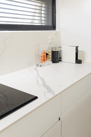 Una encimera de cocina con protector contra salpicaduras de mármol, una placa de inducción negra, una cafetera y un especiero transparente.