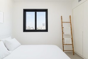 Een minimalistische slaapkamer met een bed, een raam met een zwarte omlijsting en een bamboe ladder met handdoeken.