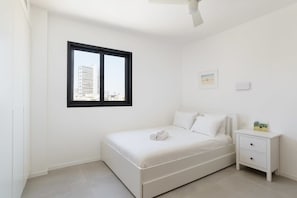 Een minimalistische slaapkamer met een bed, nachtkastje, raam en een plafondventilator.