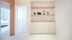 A modern, minimalist room with white walls, wooden shelves, and a bed in the adjacent room. - Spacious 4BR near the beach w Jacuzzi by HolyGuest (Tel Aviv-Yafo)