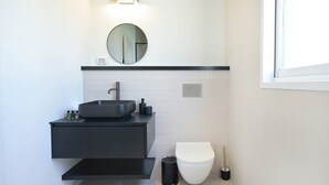 A modern bathroom with a black vanity, a round mirror, a white toilet, and a black trash bin. - Spacious 4BR near the beach w Jacuzzi by HolyGuest (Tel Aviv-Yafo)