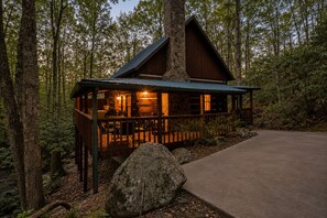 Uma cabana com chaminé de pedra, deck de madeira e entrada pavimentada.