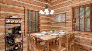 Un interior de madera con una mesa de comedor para cuatro personas, una estación de café y un cuadro en la pared.