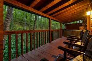 A wooden deck with a view of a forest, a hot tub, and several lounge chairs. - Summer Sale! Creek Views-2 Kings-Hot Tub-Fire Pit (Pigeon Forge)