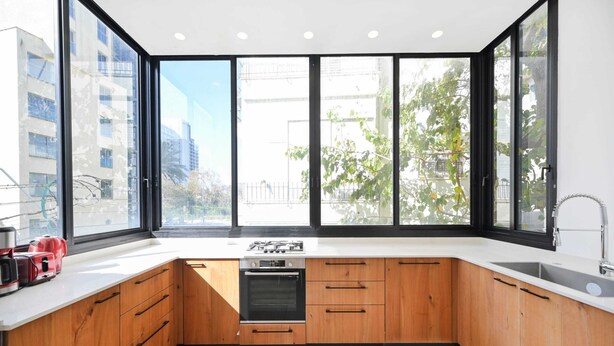 Eine moderne Küche mit Holzausstattung, einem eingebauten Backofen und einem großen Fenster mit Blick auf Gebäude und Bäume.