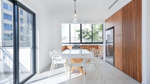 Eine moderne Küche mit einem weißen Tisch und Stühlen, Holzschränken und einem großen Fenster.