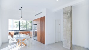 Eine moderne Küche mit weißen Schränken, einer Akzentwand aus Holz und einem Essbereich mit weißem Tisch und Stühlen.