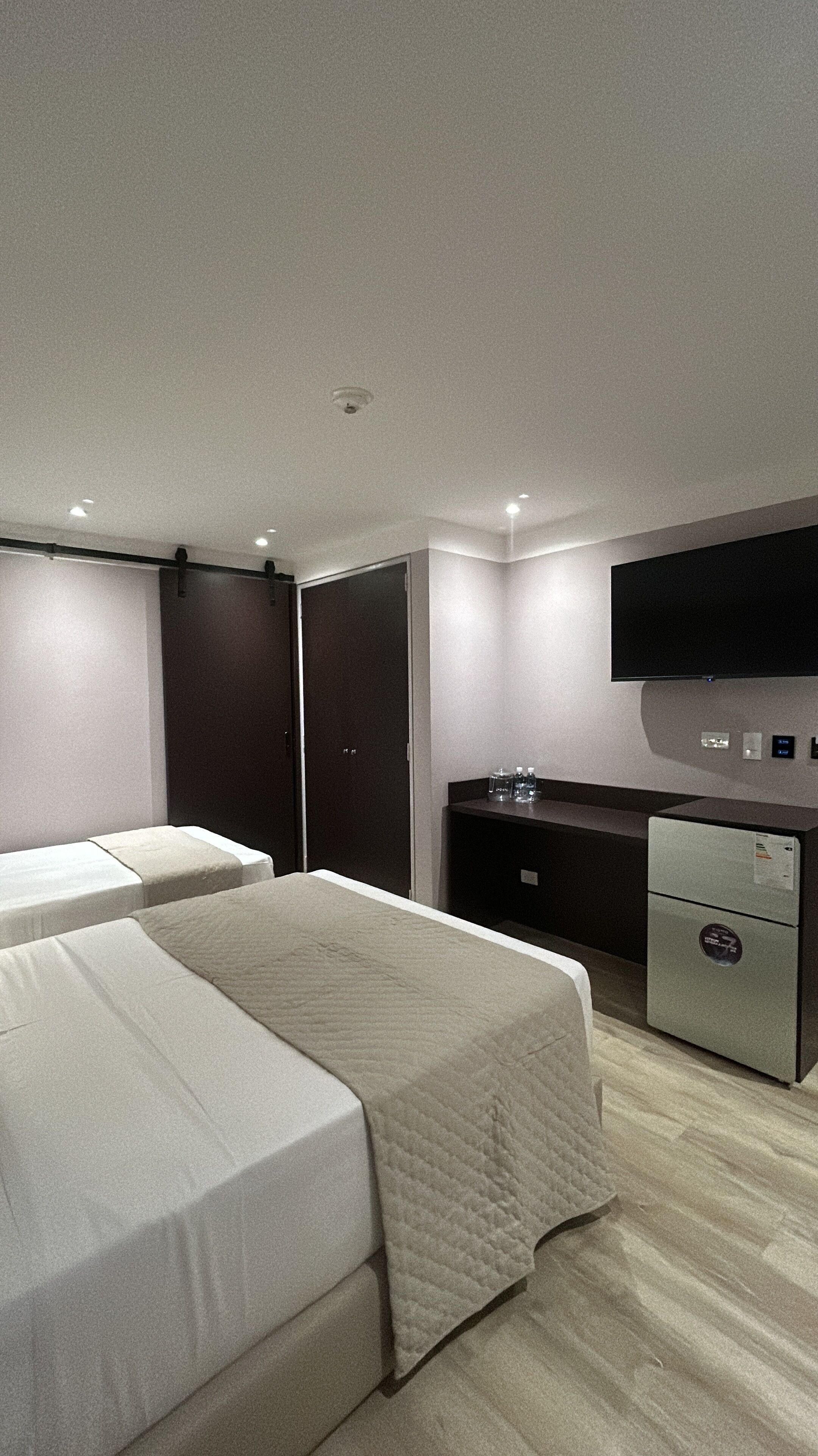 A hotel room with two beds, a desk, a flat-screen TV, and a minibar.