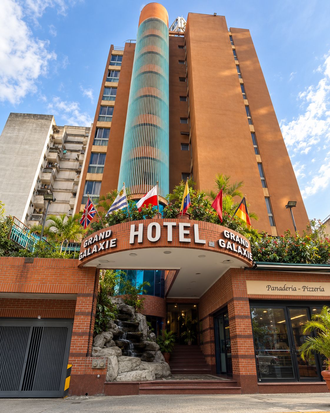 A hotel with a prominent sign, multiple flags, and a stone waterfall feature.