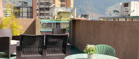 Una terraza en la azotea con mobiliario de mimbre, una mesa redonda con una planta en maceta y vistas a una cadena montañosa.