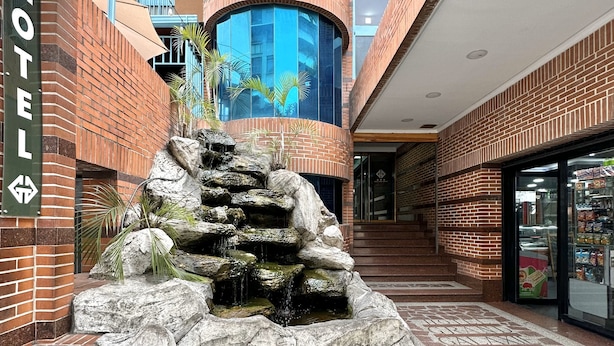 Een hotel lobby met een fontein in de vorm van een waterval, een trap naar een hoger niveau en een glazen gevel.
