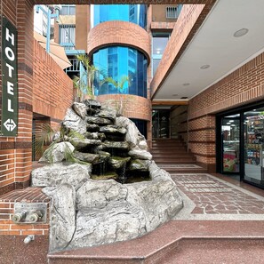 A hotel lobby with a stone waterfall feature, a staircase leading to an upper level, and a glass storefront. - Hotel Grand Galaxie (Caracas)