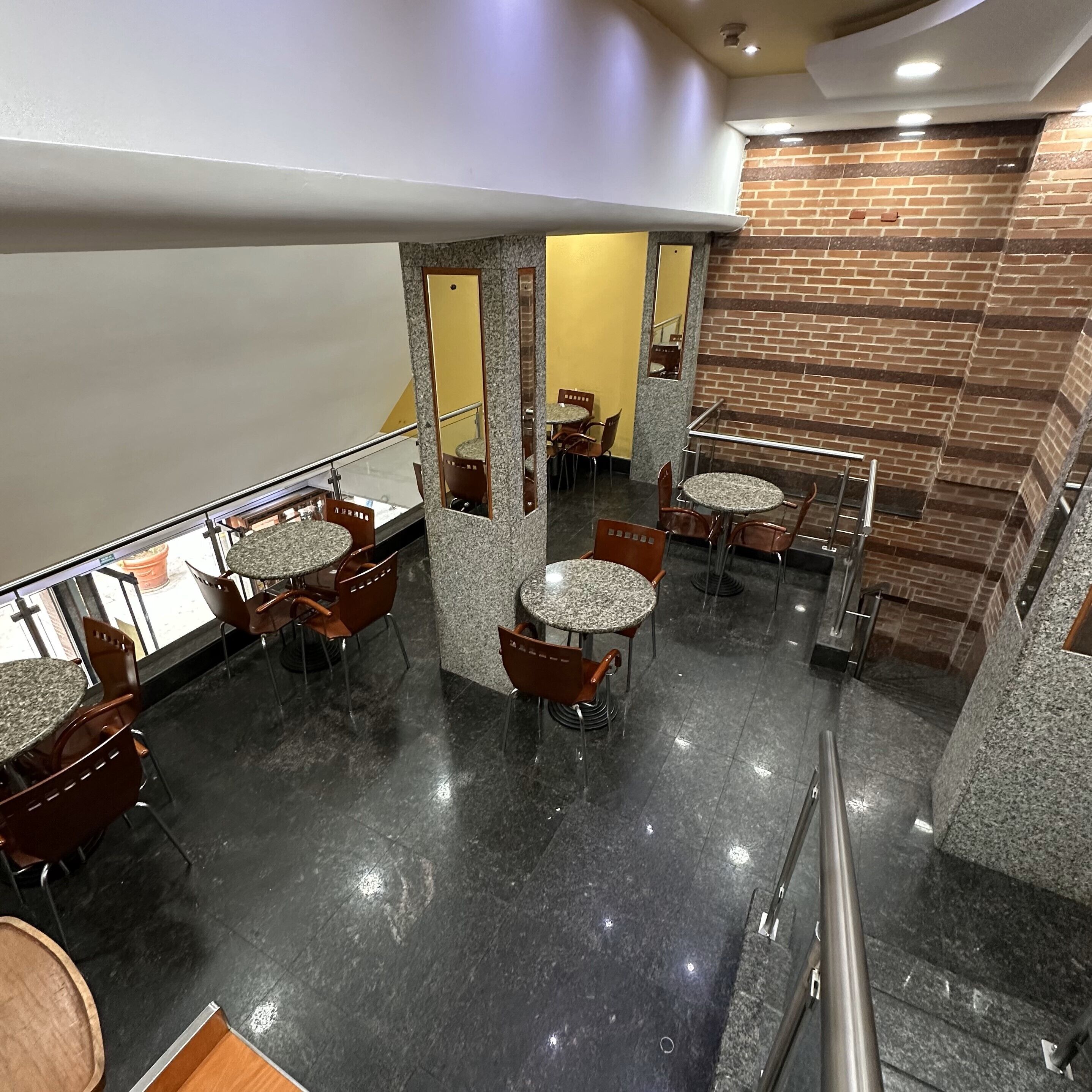 A modern indoor space with multiple seating areas, including round tables and chairs, and a staircase leading to an upper level.