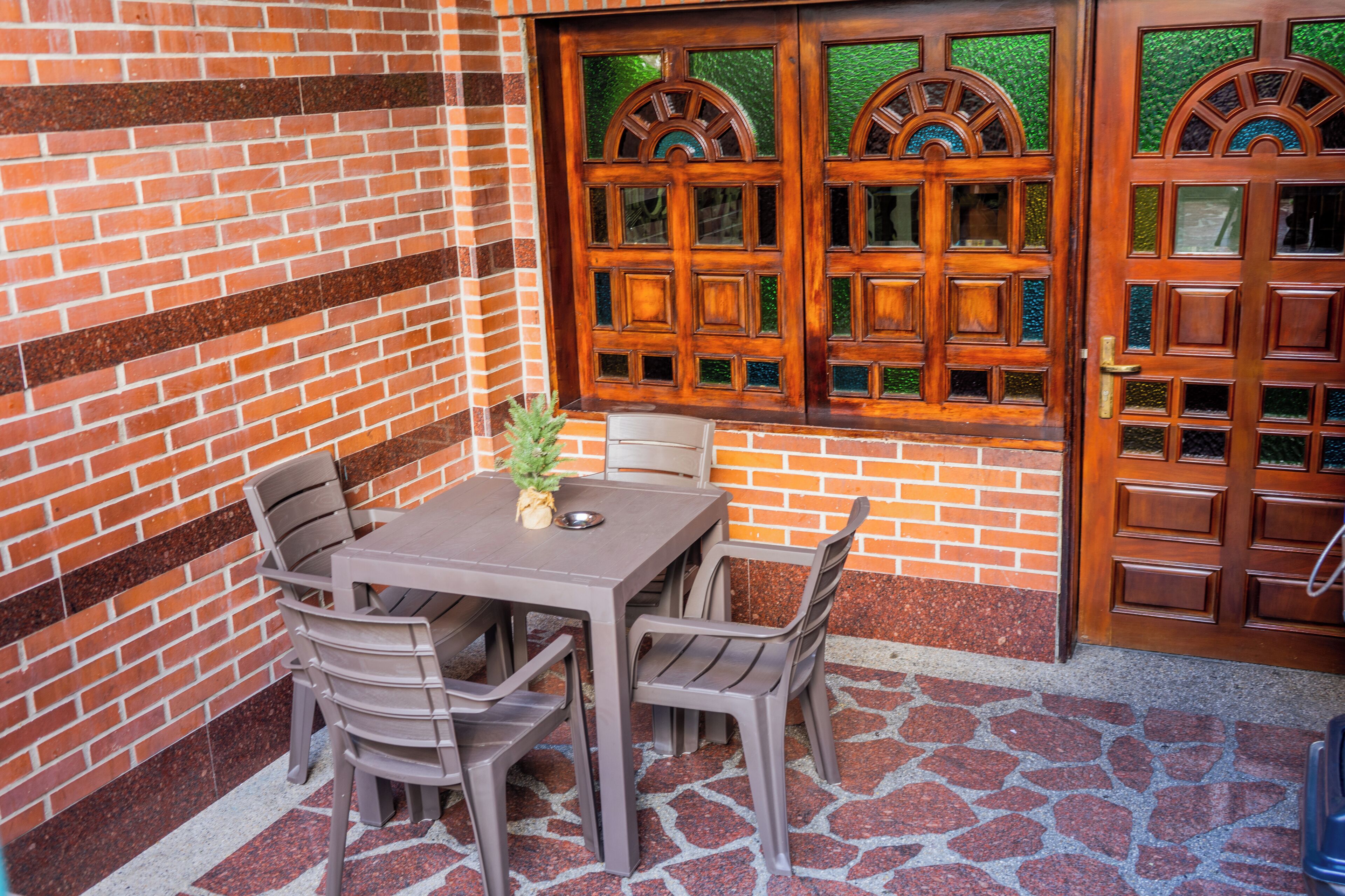 A patio with a brick wall, a wooden door with glass panels, and a table with chairs.