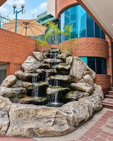 Una cascada de roca en un patio exterior, con un edificio moderno al fondo.