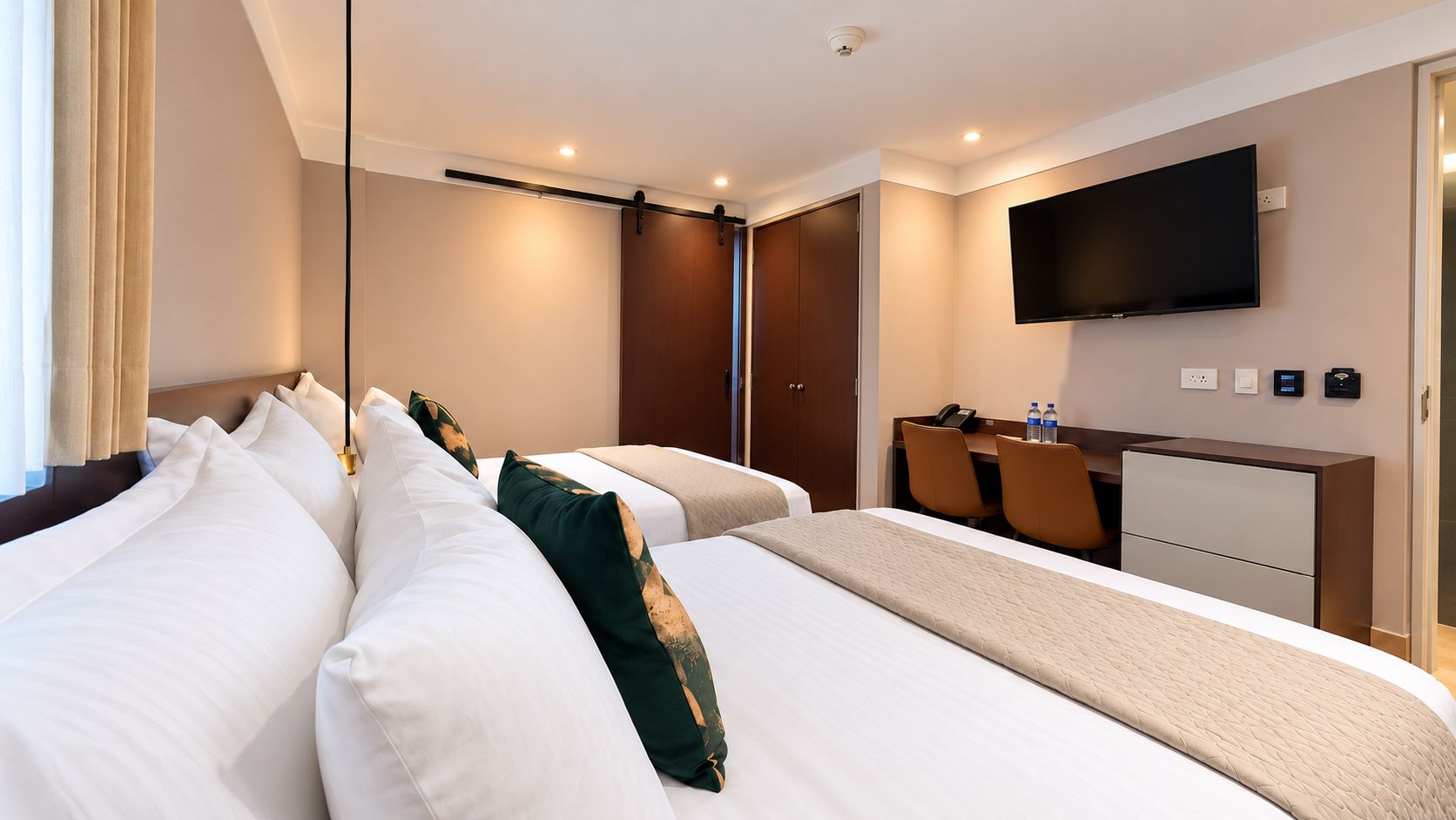 Habitación de hotel con dos camas, un escritorio, una silla, un televisor y un armario.