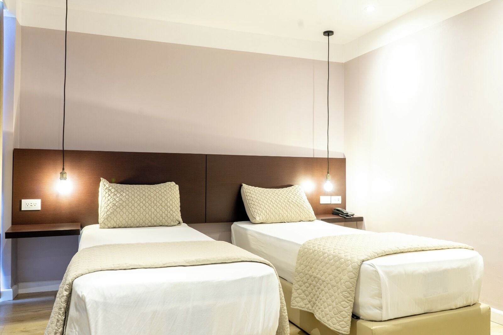 Ein Hotelzimmer mit zwei Betten, einem Holz-Kopfteil, Nachttischlampen, einem Nachttisch und einem Telefon.
