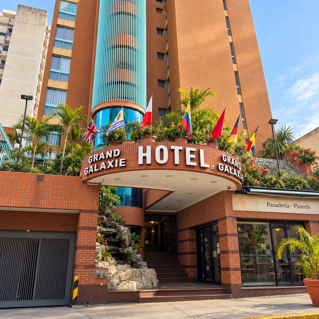 The Grand Galaxy Hotel entrance with a brick facade, a stone staircase, and multiple flags.