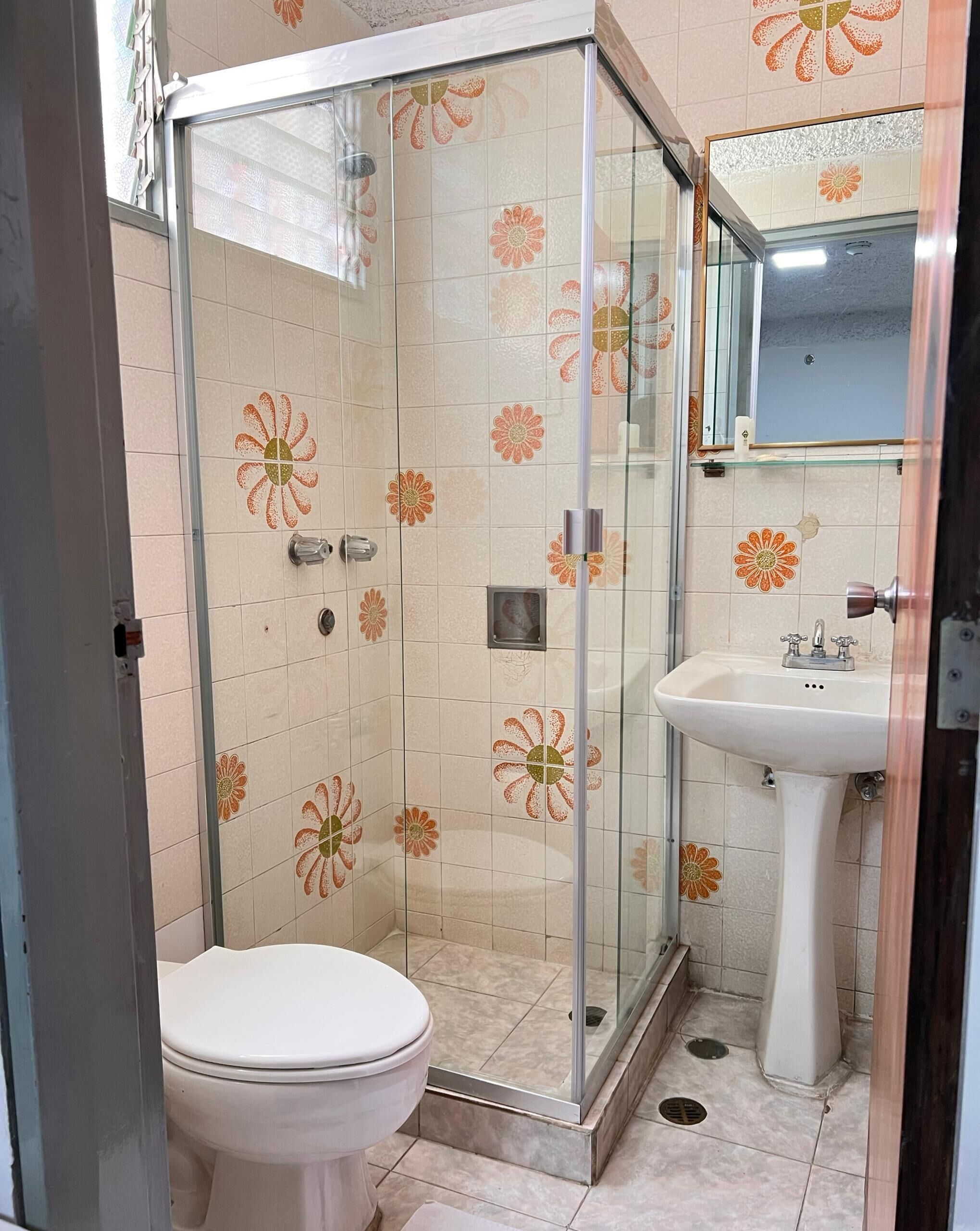 A bathroom with a glass shower enclosure, a toilet, and a sink with a mirror above it.